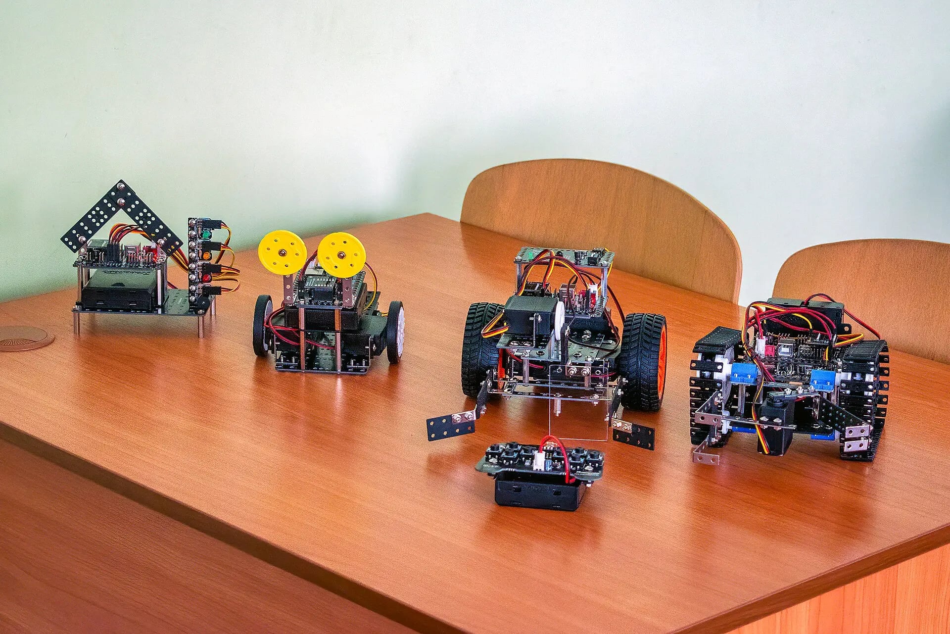 Four student-built robots lined up on a classroom table: a traffic-light rig, a two-wheel buggy, a large wheeled rover, and a tracked chassis.